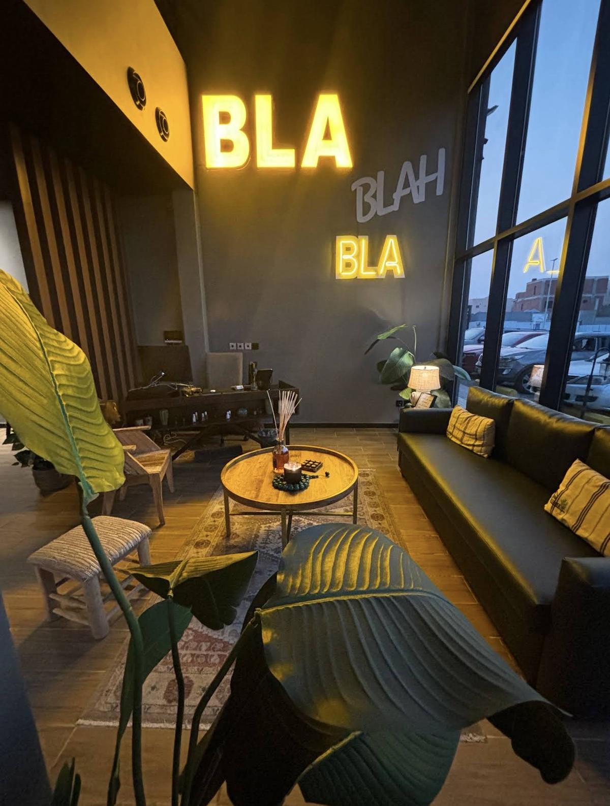 صالة ذا كورنر سبا: جدار رمادي بلوحات «BLA BLAH BLA» المضيئة، وكنبة سوداء ونباتات